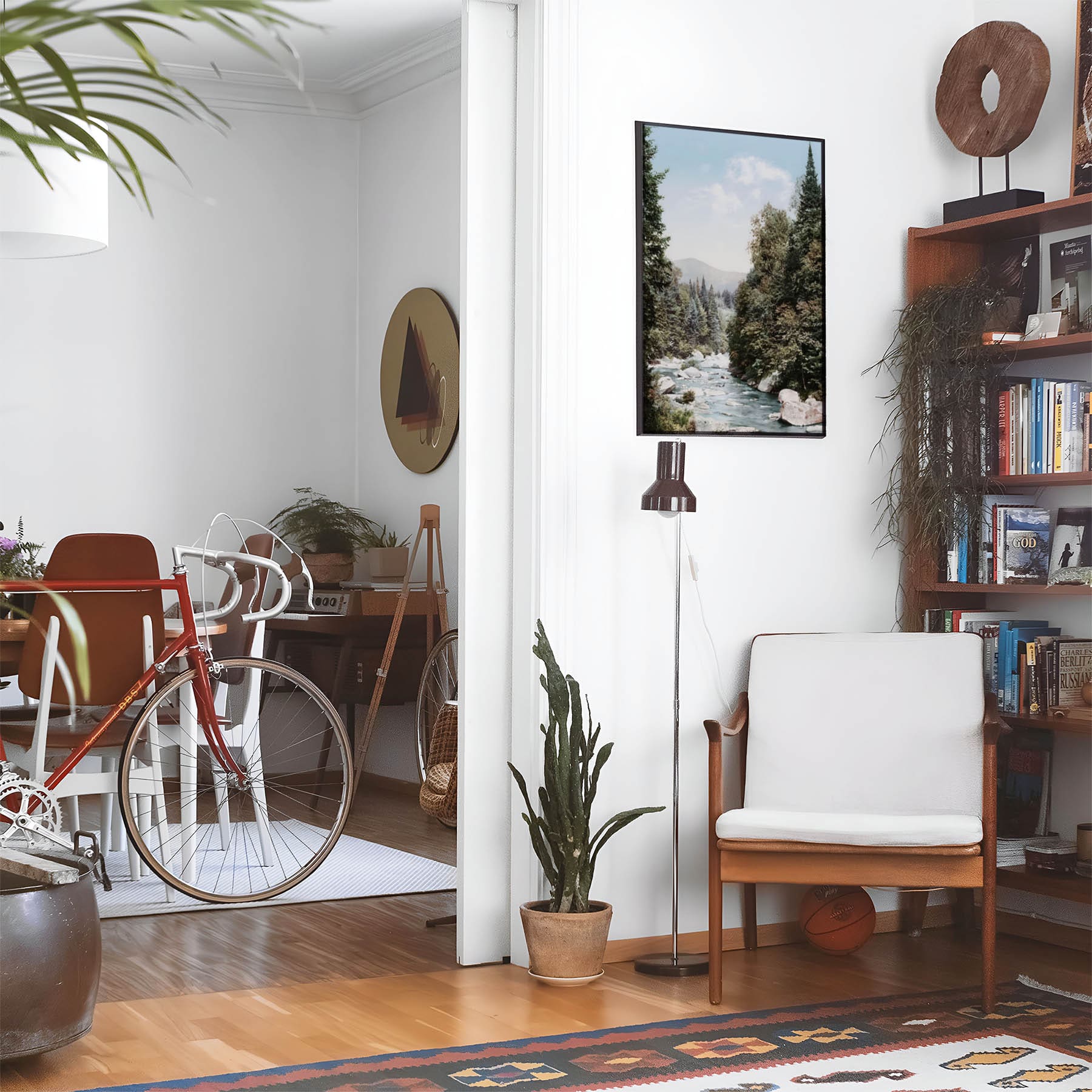 Eclectic living room with a road bike, bookshelf and house plants that features framed artwork of a Peaceful Mountain above a chair and lamp