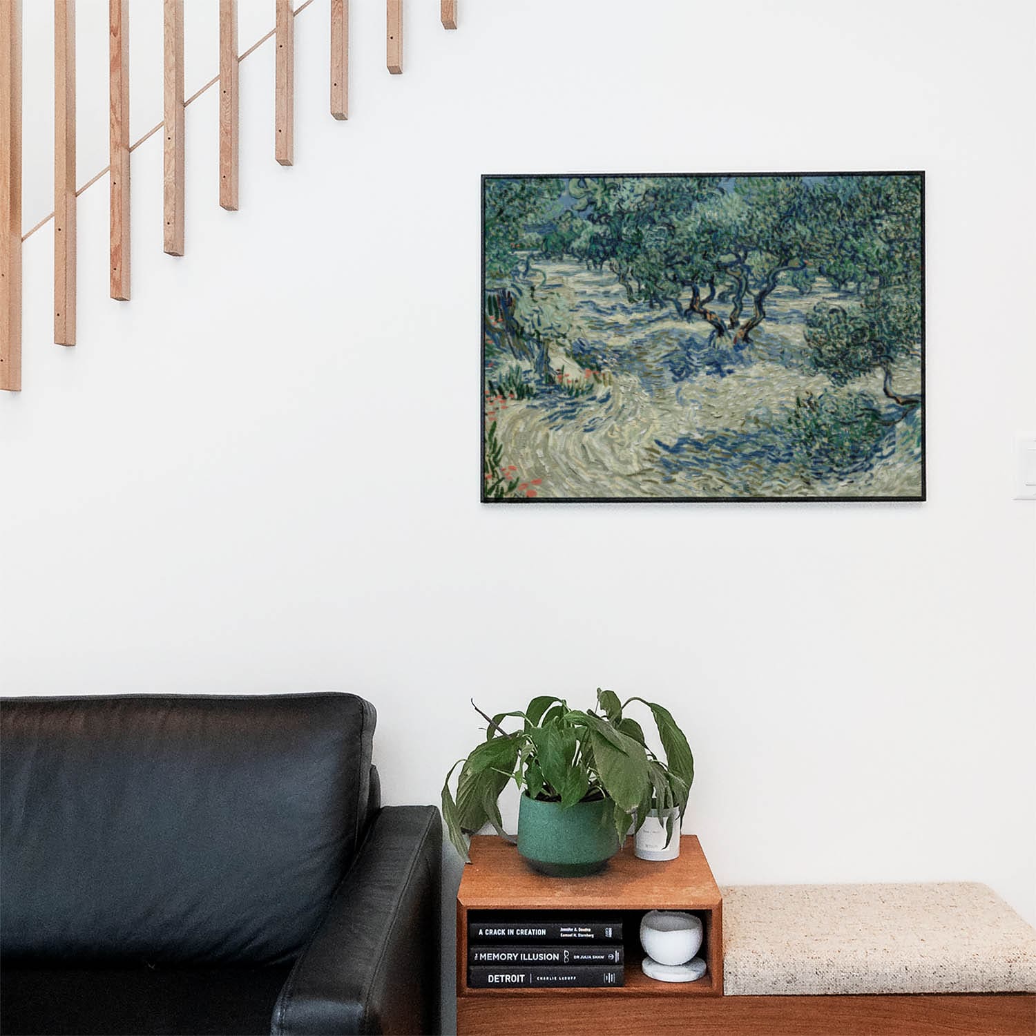 Living space with a black leather couch and table with a plant and books below a staircase featuring a framed picture of Relaxing Tree