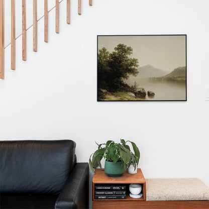 Living space with a black leather couch and table with a plant and books below a staircase featuring a framed picture of Mountian and Lake