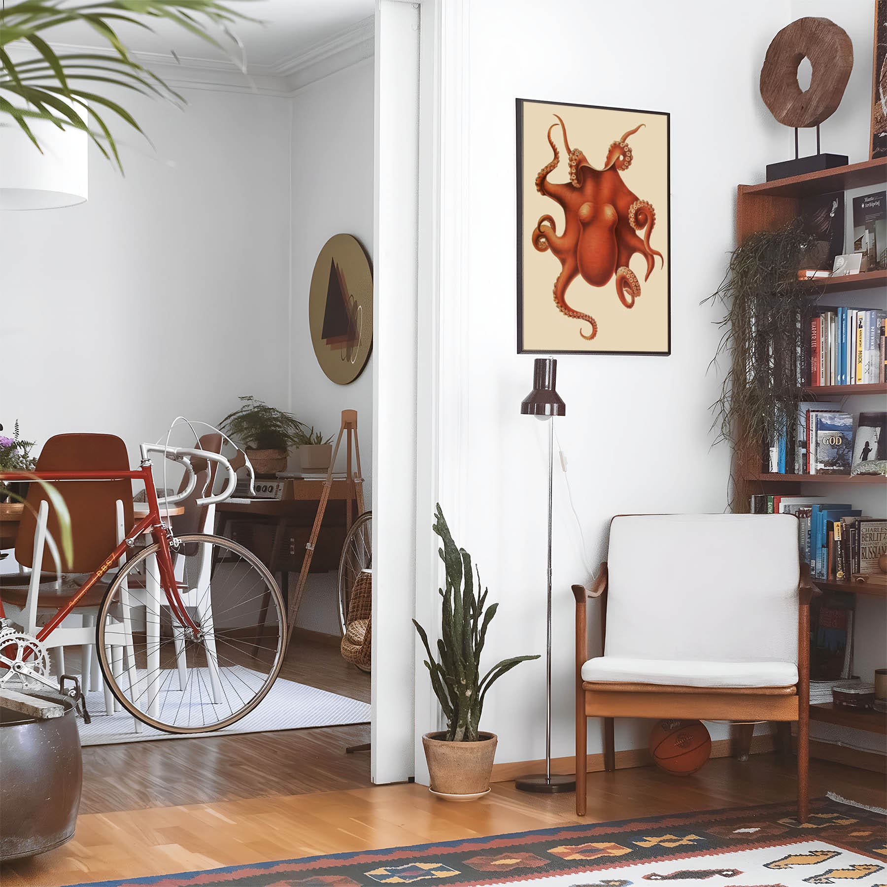 Eclectic living room with a road bike, bookshelf and house plants that features framed artwork of a Orange Red Octopus above a chair and lamp