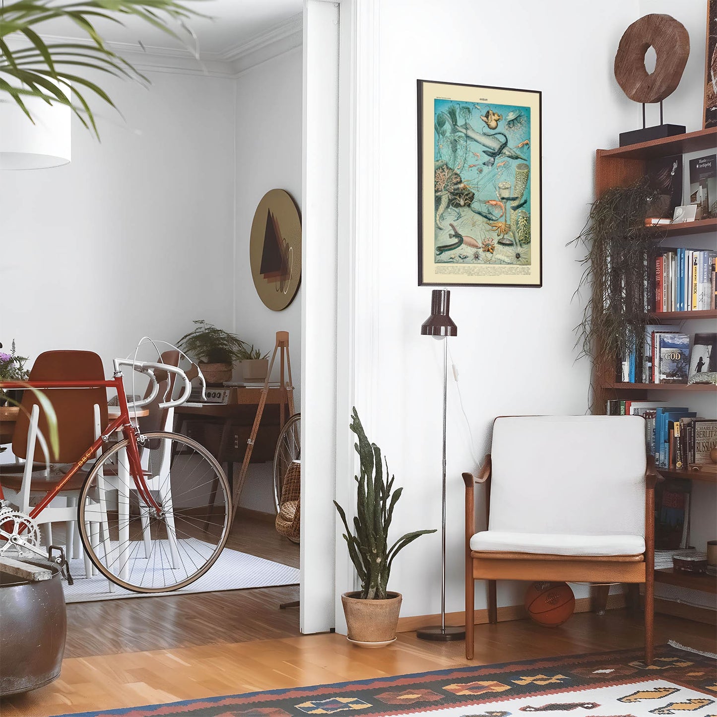 Eclectic living room with a road bike, bookshelf and house plants that features framed artwork of a Shrimp and Sharks above a chair and lamp