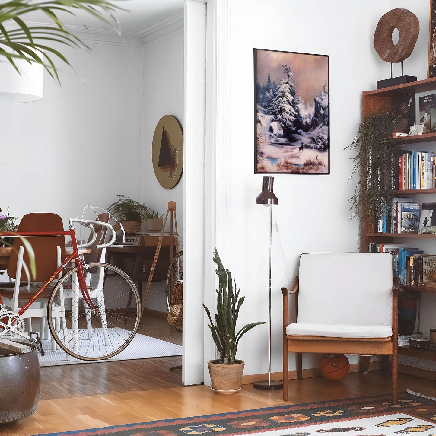 Eclectic living room with a road bike, bookshelf and house plants that features framed artwork of a Forest Covered in Snow above a chair and lamp