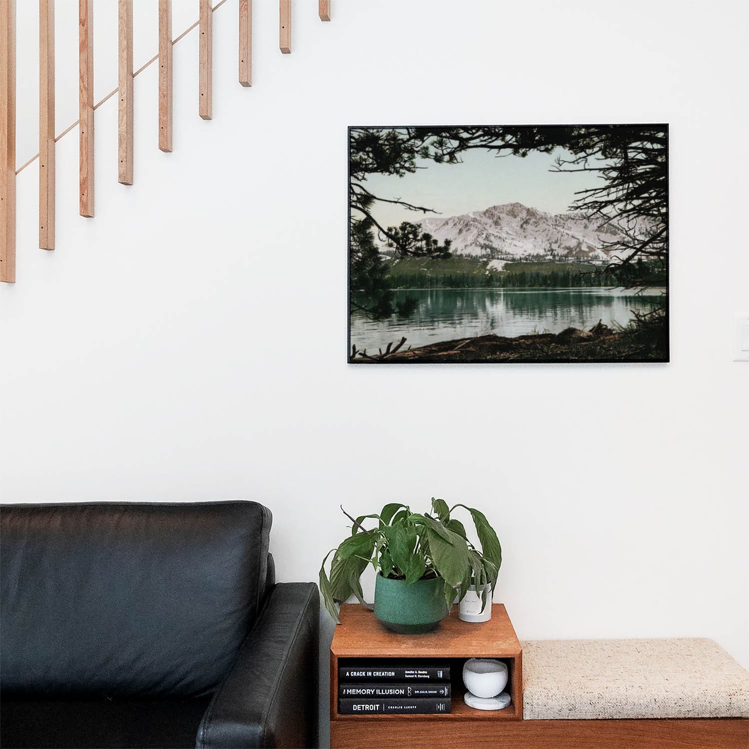 Living space with a black leather couch and table with a plant and books below a staircase featuring a framed picture of Lake in the Wilderness