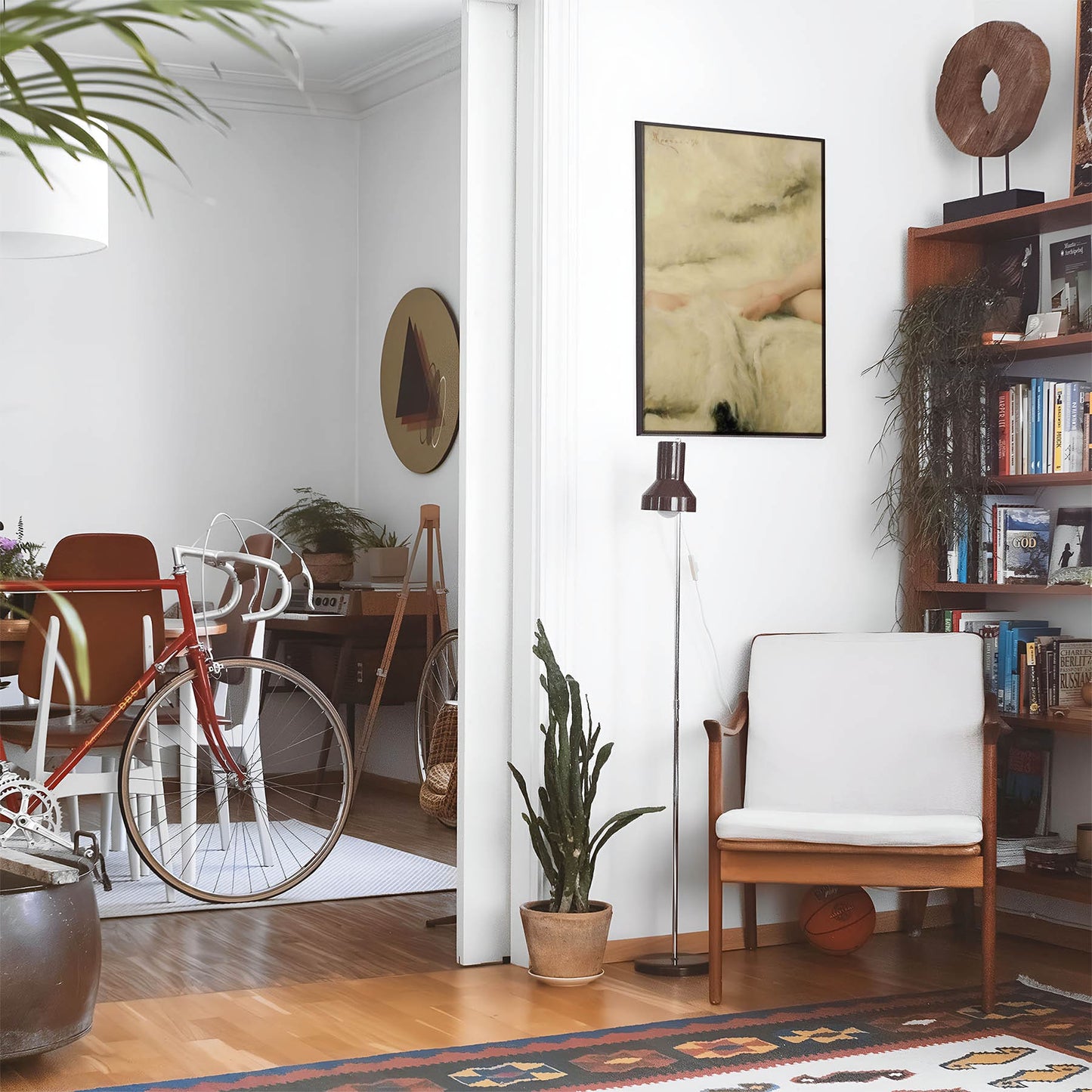 Eclectic living room with a road bike, bookshelf and house plants that features framed artwork of a Womans Legs on a White Fur Blanket above a chair and lamp