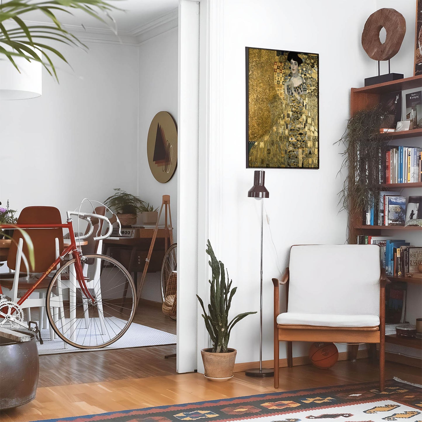 Eclectic living room with a road bike, bookshelf and house plants that features framed artwork of a Art Nouveau Symbolic above a chair and lamp