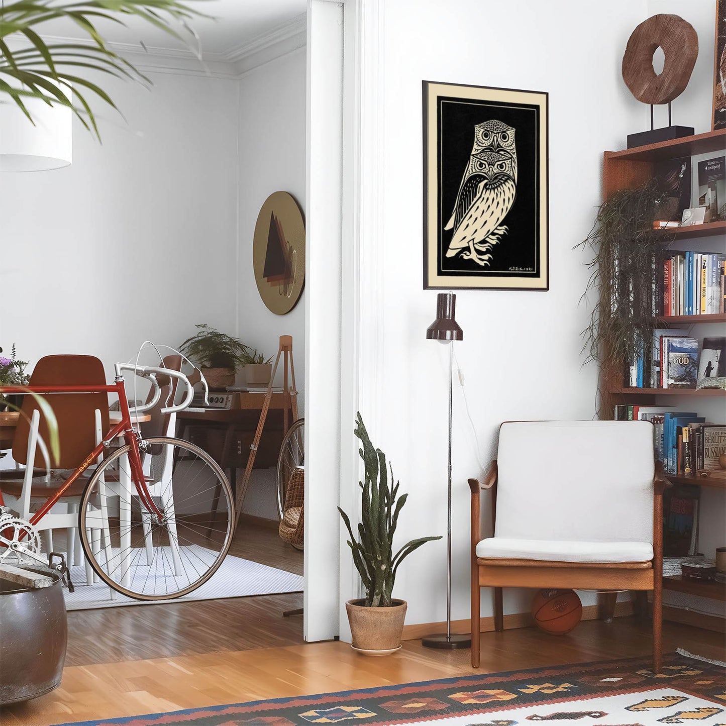 Eclectic living room with a road bike, bookshelf and house plants that features framed artwork of a Black and White Owls above a chair and lamp