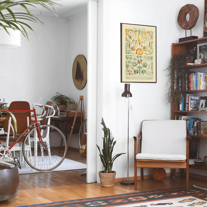 Eclectic living room with a road bike, bookshelf and house plants that features framed artwork of a Garden Variety above a chair and lamp