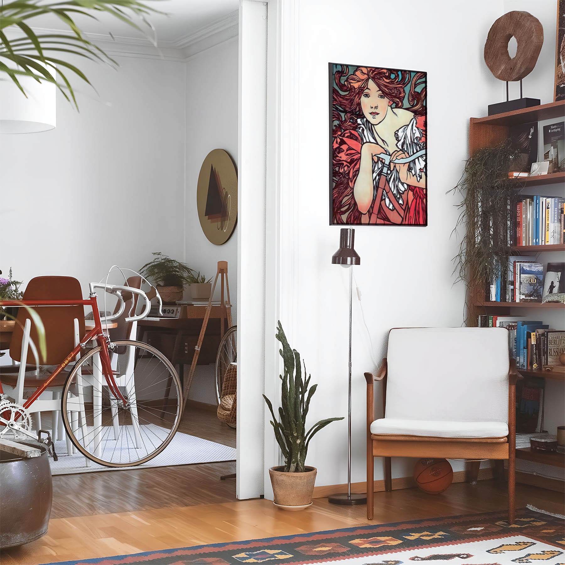 Eclectic living room with a road bike, bookshelf and house plants that features framed artwork of a Woman with Flowing Red Hair on a Bicycle above a chair and lamp