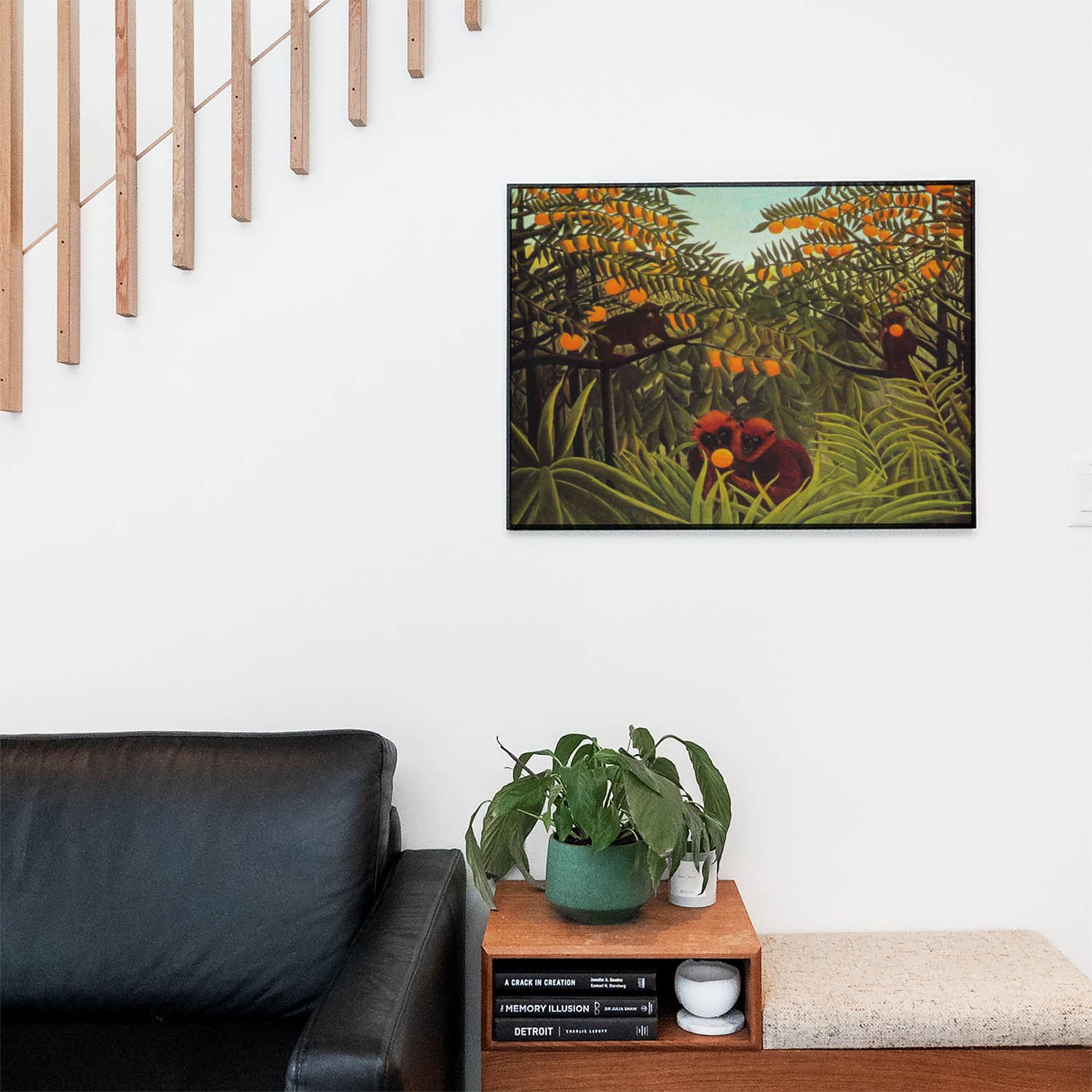 Living space with a black leather couch and table with a plant and books below a staircase featuring a framed picture of Lush Jungle