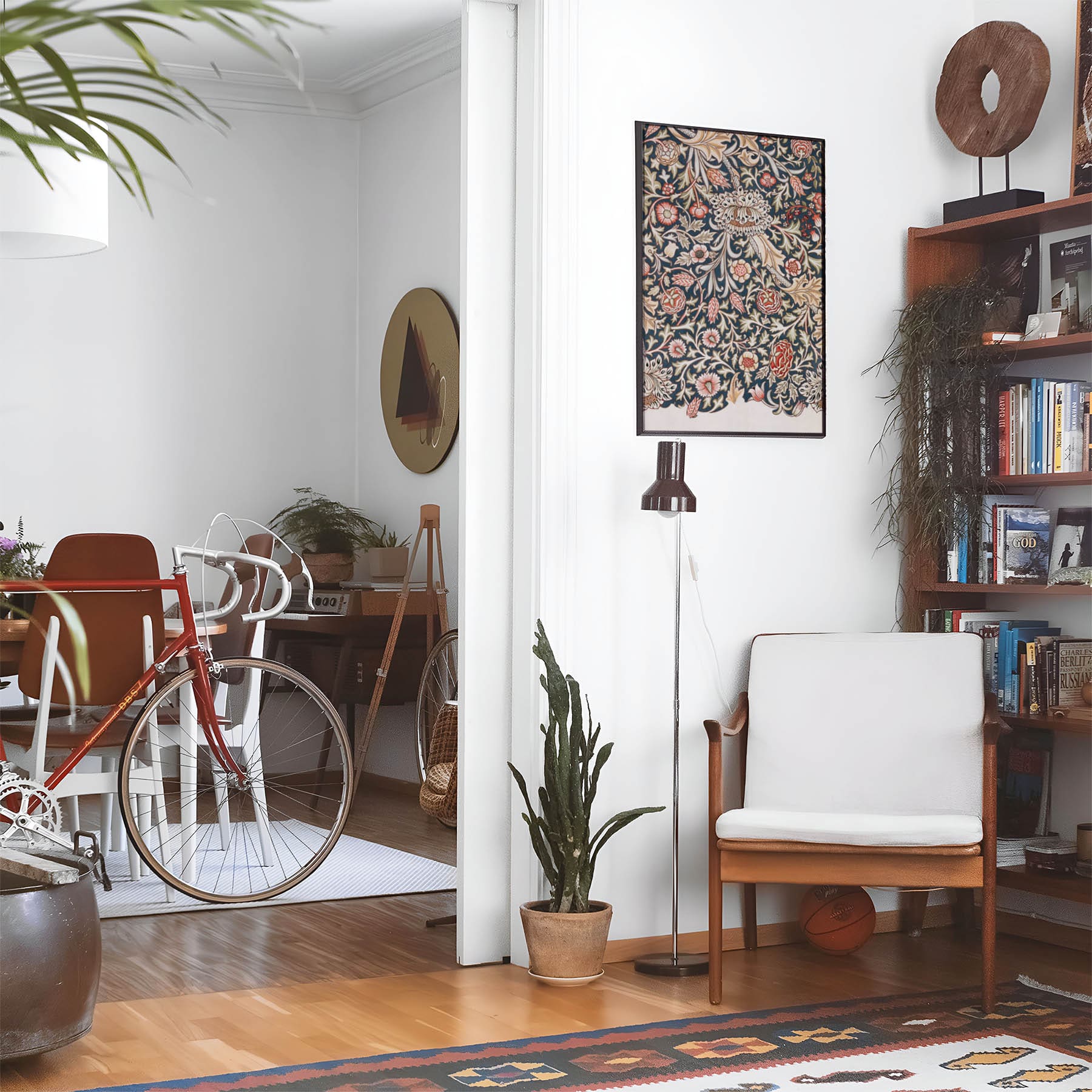 Eclectic living room with a road bike, bookshelf and house plants that features framed artwork of a Floral above a chair and lamp