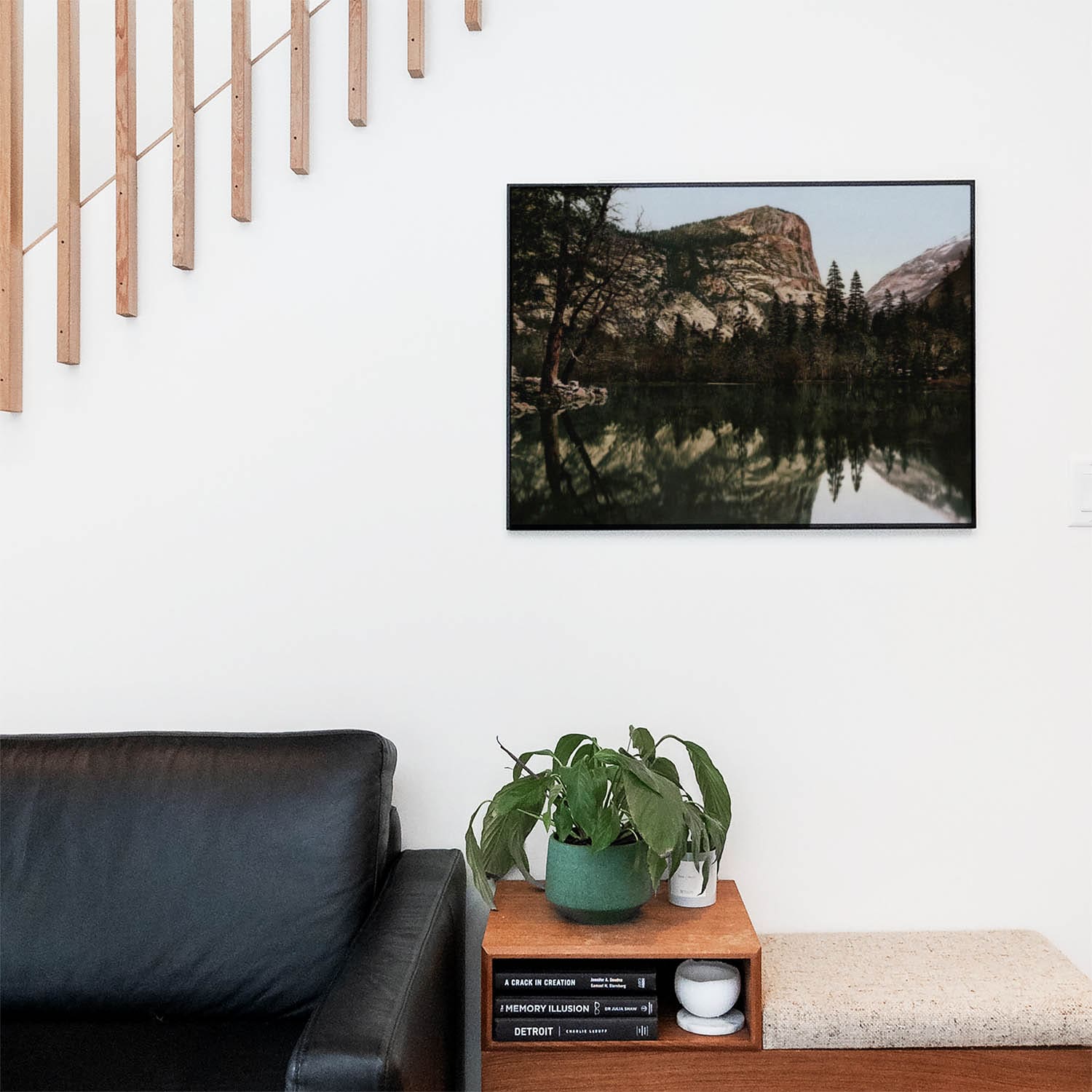 Living space with a black leather couch and table with a plant and books below a staircase featuring a framed picture of Mt. Watkins and Half Dome