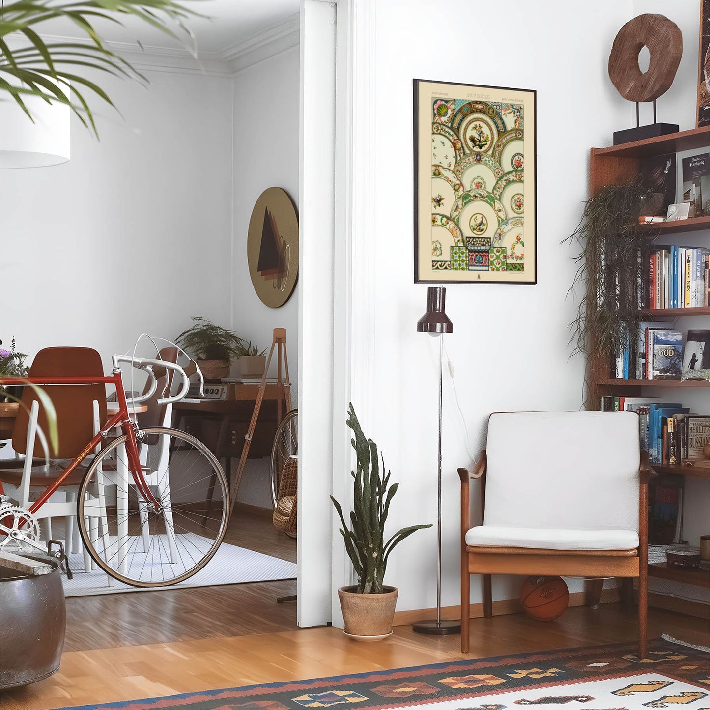 Eclectic living room with a road bike, bookshelf and house plants that features framed artwork of a Ornamental Plates above a chair and lamp