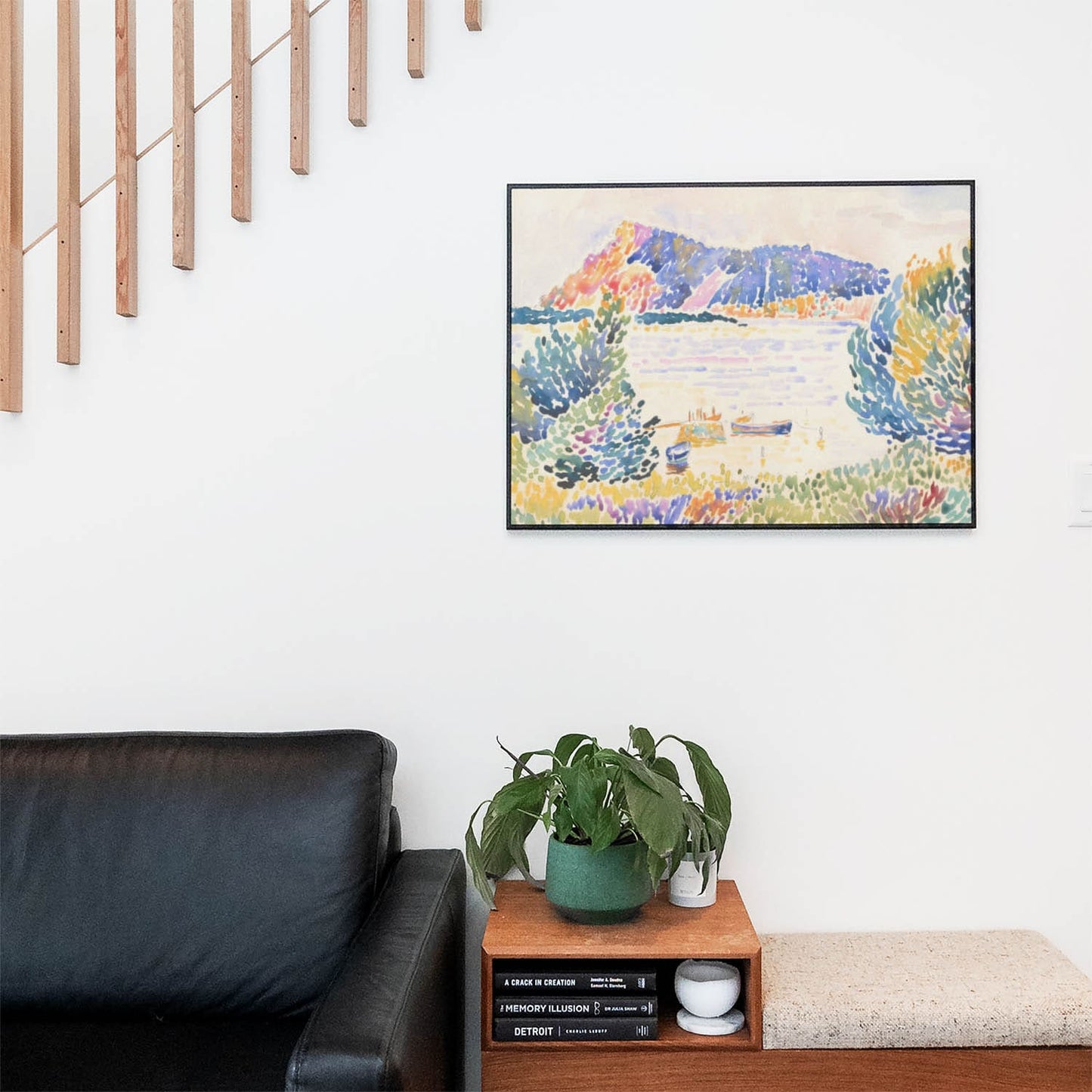 Living space with a black leather couch and table with a plant and books below a staircase featuring a framed picture of Calm and Peaceful