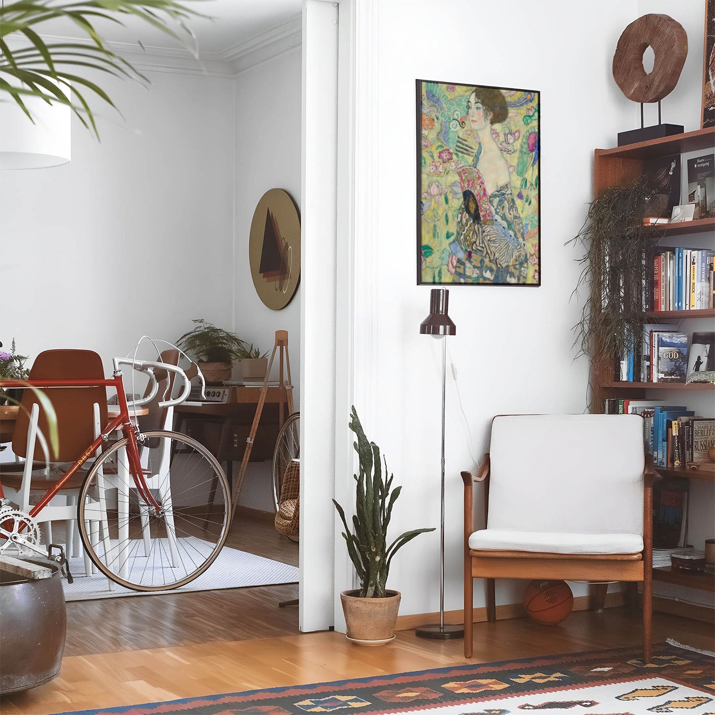 Eclectic living room with a road bike, bookshelf and house plants that features framed artwork of a Light and Floral above a chair and lamp