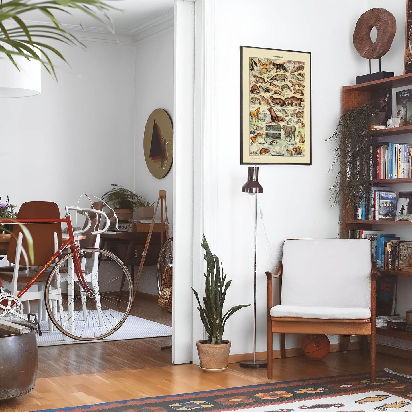 Eclectic living room with a road bike, bookshelf and house plants that features framed artwork of a Cute Animal above a chair and lamp