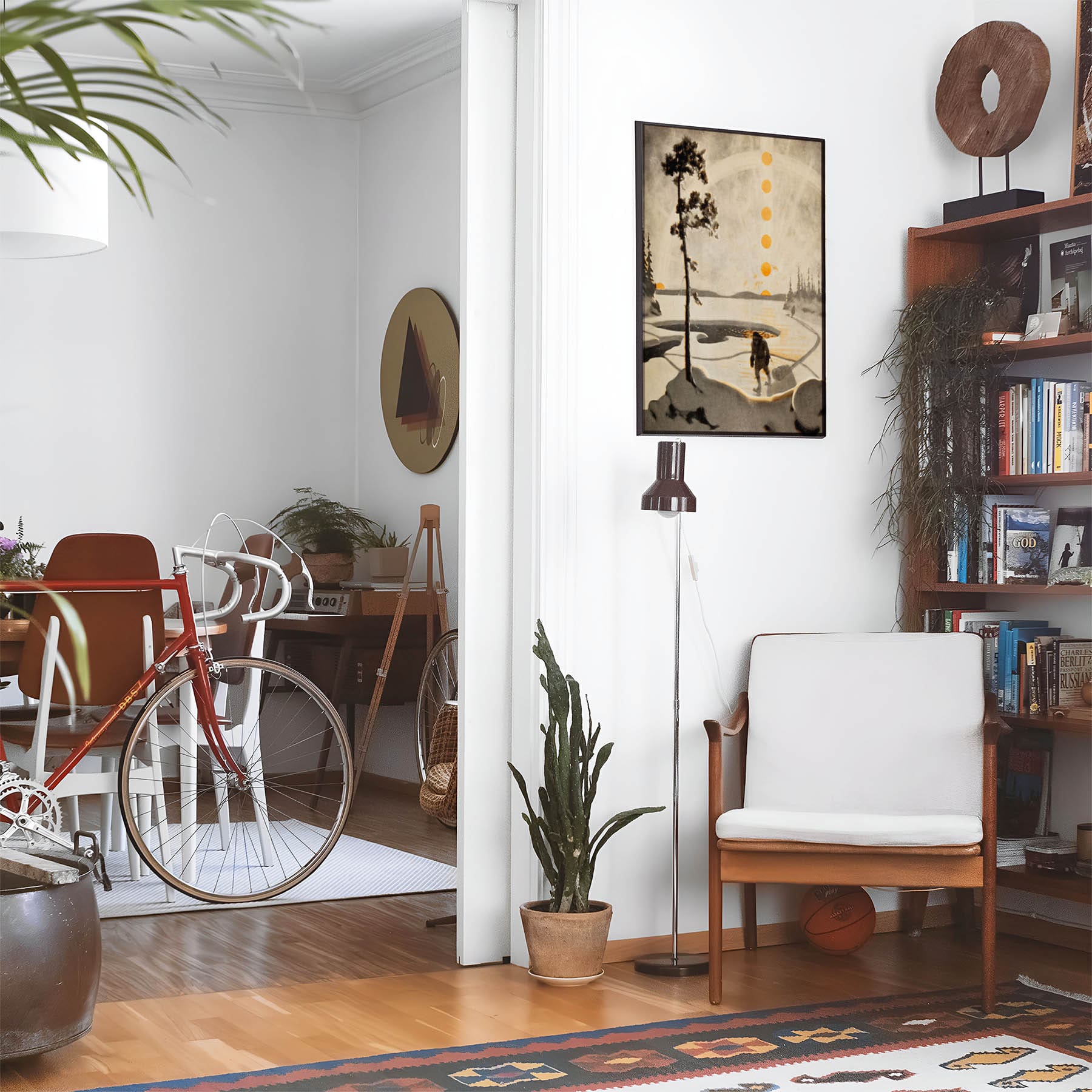 Eclectic living room with a road bike, bookshelf and house plants that features framed artwork of a Snowy Figure and the Sun above a chair and lamp