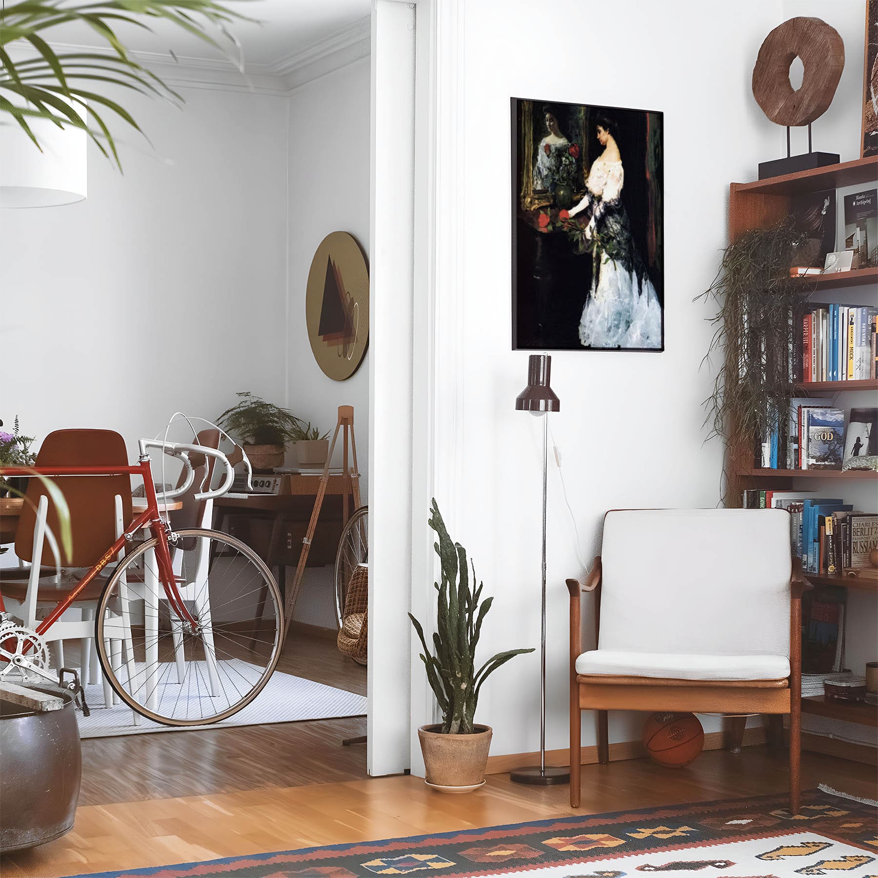 Eclectic living room with a road bike, bookshelf and house plants that features framed artwork of a Dark Victorian above a chair and lamp